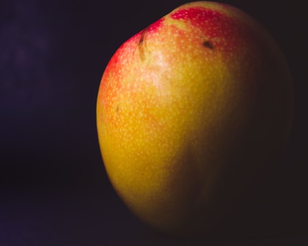 A close-up image of a ripe mango with a smooth yellow and red skin, highlighted against a dark background, enhancing its vivid colors and textures.