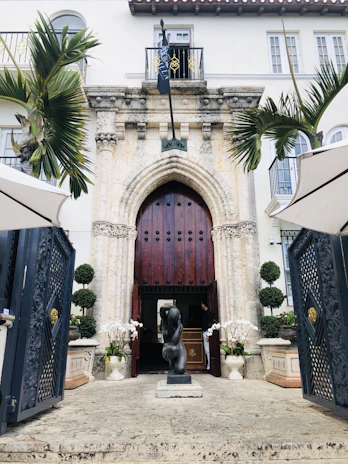 Elegant estate entrance featuring grand wooden doors and lush greenery.