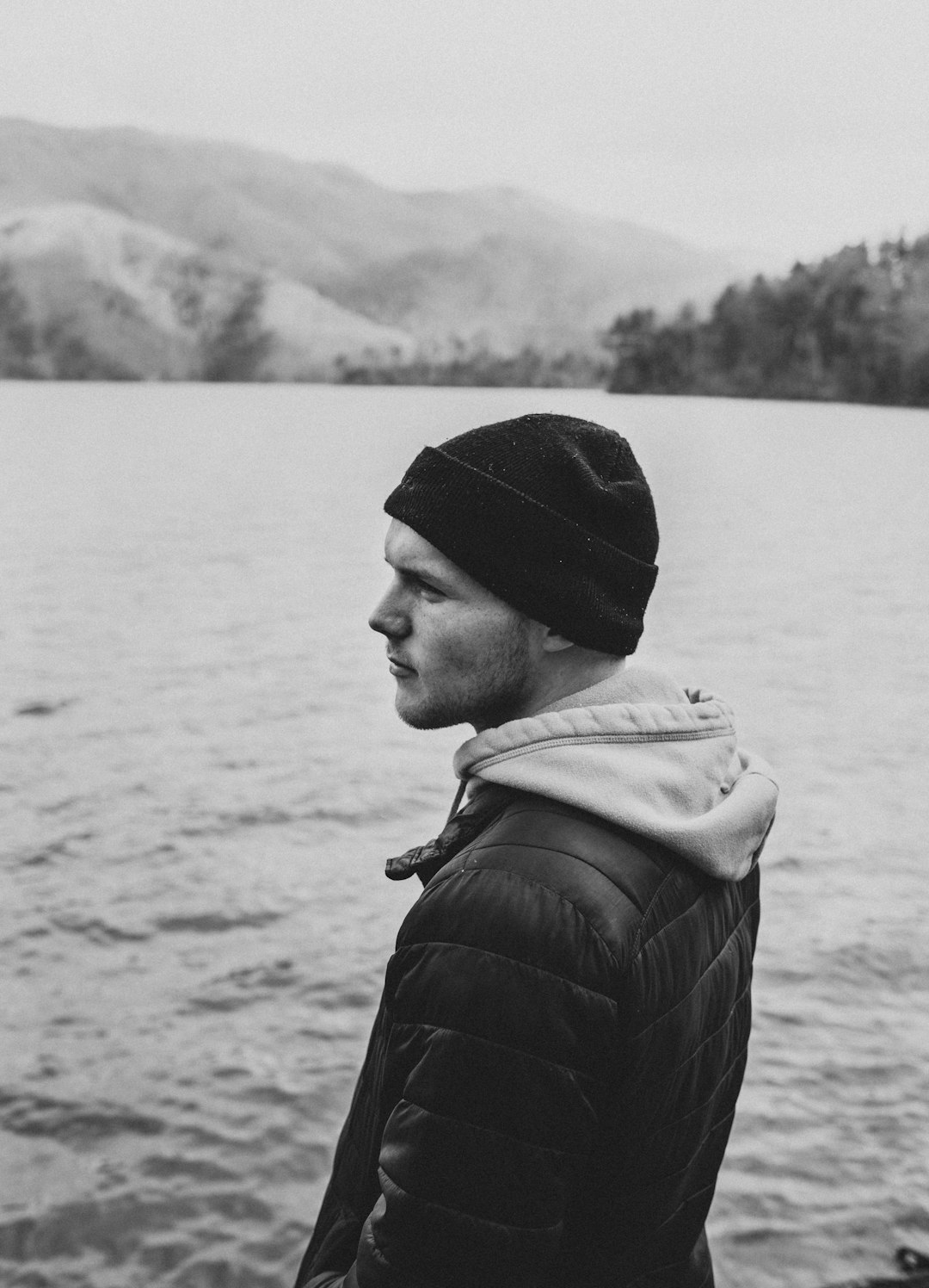 grayscale photography of man standing beside body of water