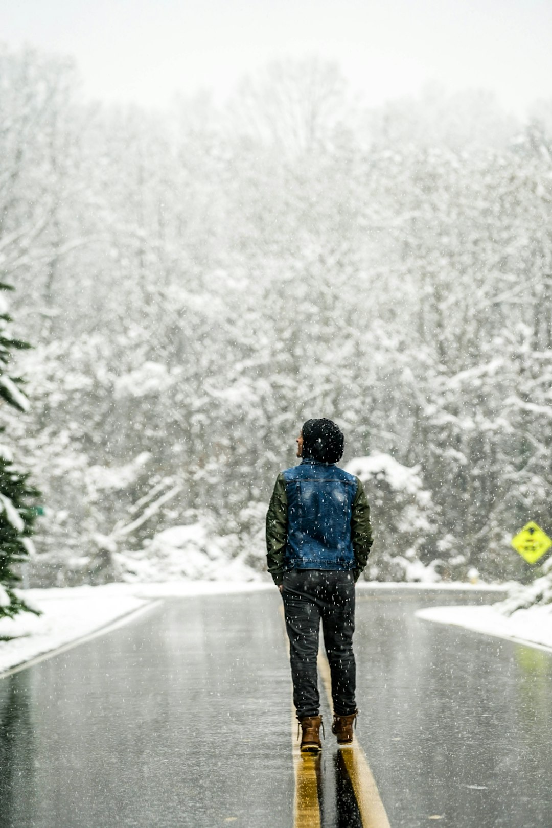 person waering blue and black jacket standing on the middle og asphalt road while raining snow