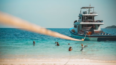 Boat anchored near a sandy bank with people enjoying jet-ski and paddleboarding under a bright sky.