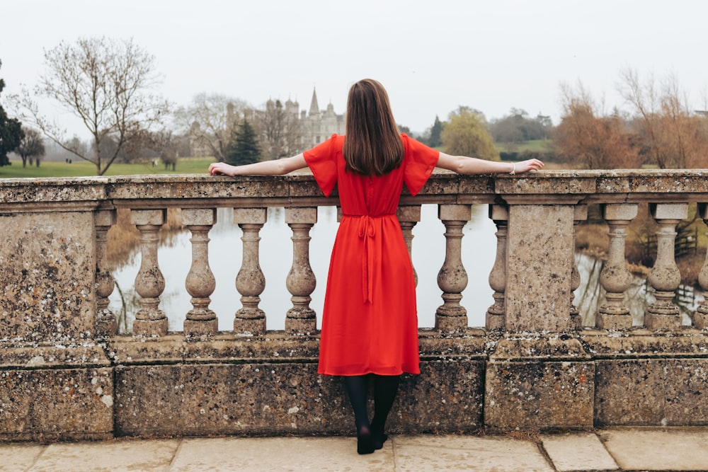 woman in red dress looking at body of water and trees during daytime