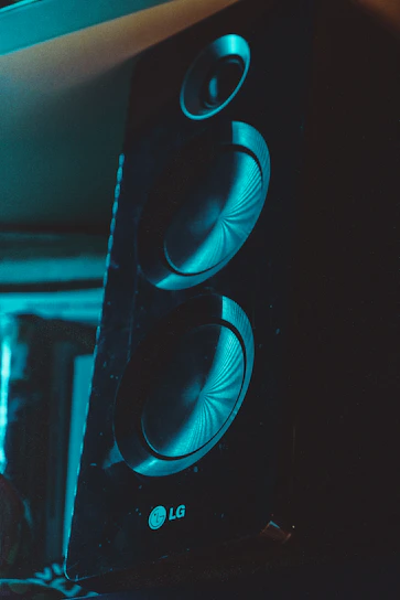 Close-up of a sleek, metallic luxury speaker with glowing navy blue accents against a deep black background.