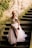 A person wearing an elegant, flowing gown with intricate floral embroidery on the bodice walks down a stone staircase. The stone wall is partially covered in greenery, adding a natural element to the setting.