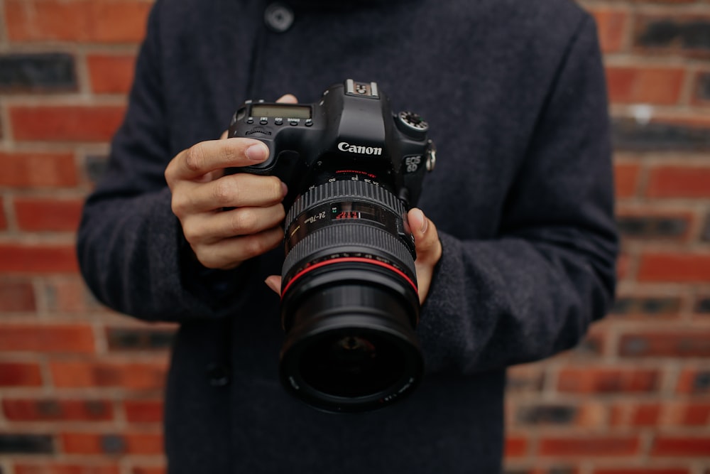 Foto einer Person mit flachem Fokus, die eine schwarze Canon DSLR-Kamera hält