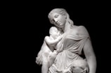 A marble statue of a mother gently holding her newborn, inspired by Swedish Grace aesthetics.