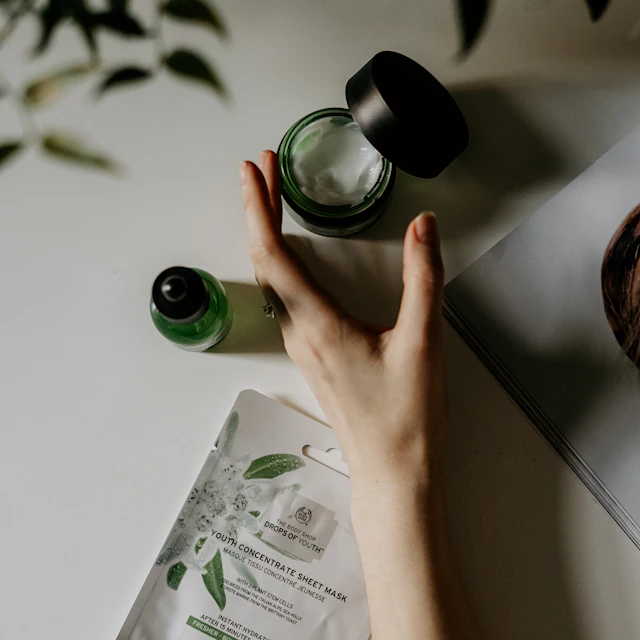 A hand reaching toward a jar of cream, a serum bottle and a sheet mask