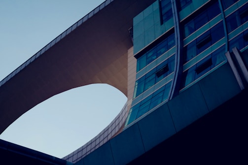 A modern architectural structure with smooth curves and a bridge-like feature connecting two sections of the building. The design incorporates extensive use of glass panels and steel, creating a reflective and sleek appearance.