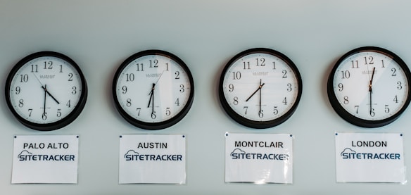 Four wall clocks are mounted in a row, each displaying different times. Below each clock, there are signs labeled 'PALO ALTO', 'AUSTIN', 'MONTCLAIR', and 'LONDON' with the word 'SITETRACKER' beneath each city name. The clocks have black frames and white clock faces with black numerals.