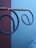 Two spiral mosquito coils are suspended horizontally on a stick. They are partially burnt and the tips glow red. The background consists of a plain wall, partially visible in red and light blue.