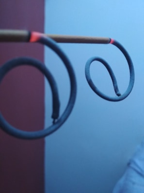 Two spiral mosquito coils are suspended horizontally on a stick. They are partially burnt and the tips glow red. The background consists of a plain wall, partially visible in red and light blue.