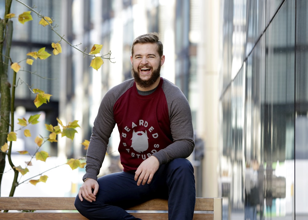 man wearing red and gray long-sleeved shirt sitting of bench