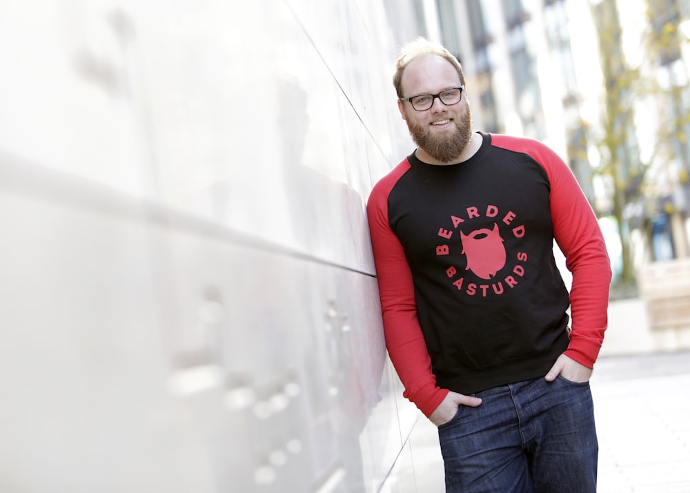 man wearing black and red long-sleeved shirt leaning on white wall