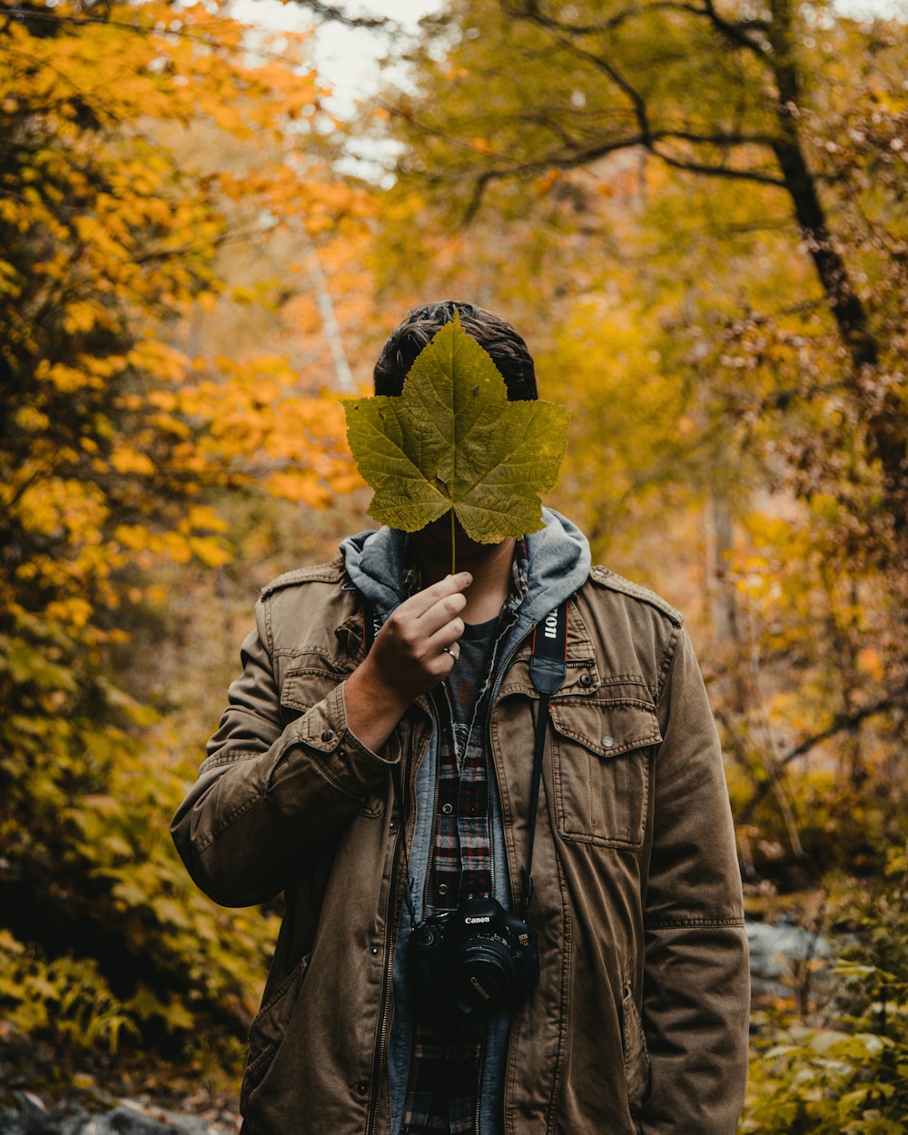 man holding green leaf covering his face