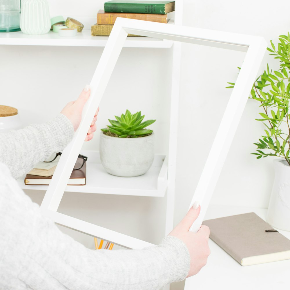 persona sosteniendo un marco de madera blanco