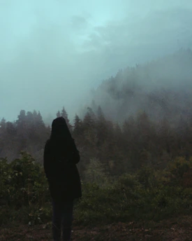 Moody cinematic silhouette of a man standing at dawn in a misty forest, golden light trails swirling around him.