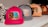 A row of colorful caps placed on a white surface. The closest cap is bright pink with a patch featuring a blue rose and leopard print design. The other caps are in shades of gray, peach, and maroon, each with different decorative patches.