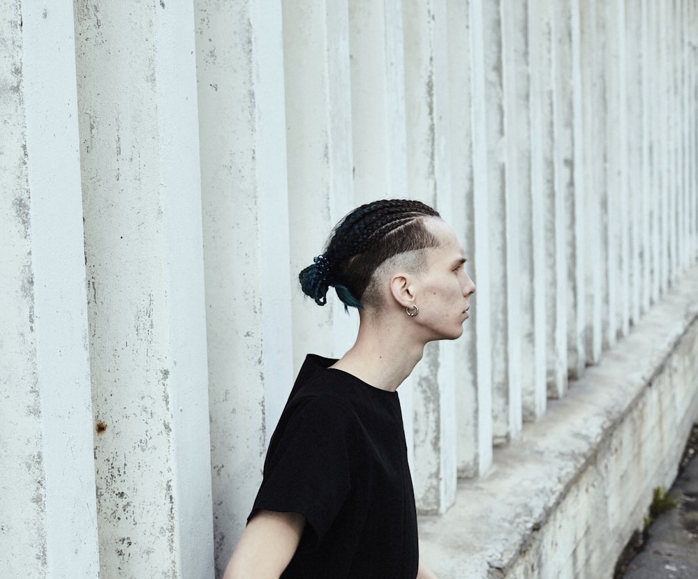 man wearing black crew-neck shirt standing beside white painted wall