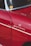 A close-up view of a vintage car that is predominantly red with chrome accents. There is a sticker or emblem on the car reading 'Weekend Heroes' and a small round yellow sticker on the window. The surface of the car reflects light, showing the smoothness and shine of the paint.
