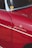 A close-up view of a vintage car that is predominantly red with chrome accents. There is a sticker or emblem on the car reading 'Weekend Heroes' and a small round yellow sticker on the window. The surface of the car reflects light, showing the smoothness and shine of the paint.