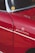 A close-up view of a vintage car that is predominantly red with chrome accents. There is a sticker or emblem on the car reading 'Weekend Heroes' and a small round yellow sticker on the window. The surface of the car reflects light, showing the smoothness and shine of the paint.