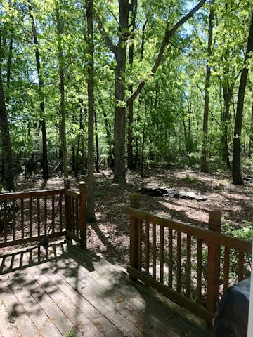 A smiling craftsman installing a custom wooden railing on a sunlit deck surrounded by green plants.