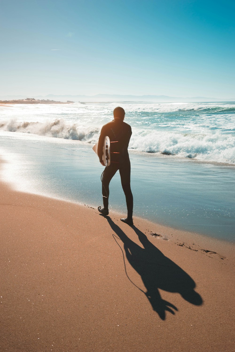 man in wetsuit holding surfboard on shore