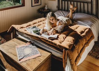 woman lying on bed while reading book