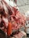 A butcher's shop displaying a variety of raw meats, including whole pig heads, hanging carcasses, and sausages. There is a man in a white uniform working behind the counter, surrounded by various cuts of meat on metal shelves.