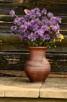 A wide mouth ceramic vase filled with dried wildflowers on a rustic wooden table.