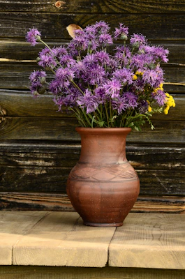 A close-up of a textured clay vase with earthy tones, filled with fresh wildflowers, evoking slow living.