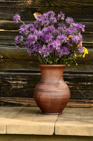 An elegant ceramic vase filled with fresh wildflowers on a rustic wooden table.