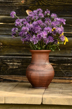 A wide mouth ceramic vase filled with dried wildflowers on a rustic wooden table.