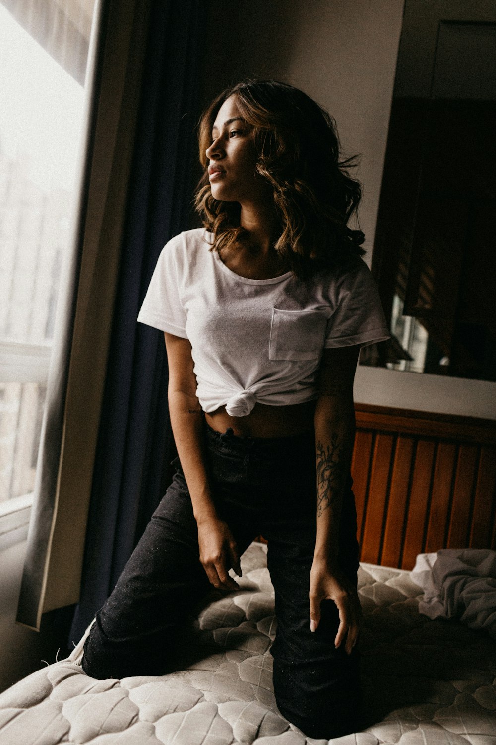 woman kneeling on bed beside window