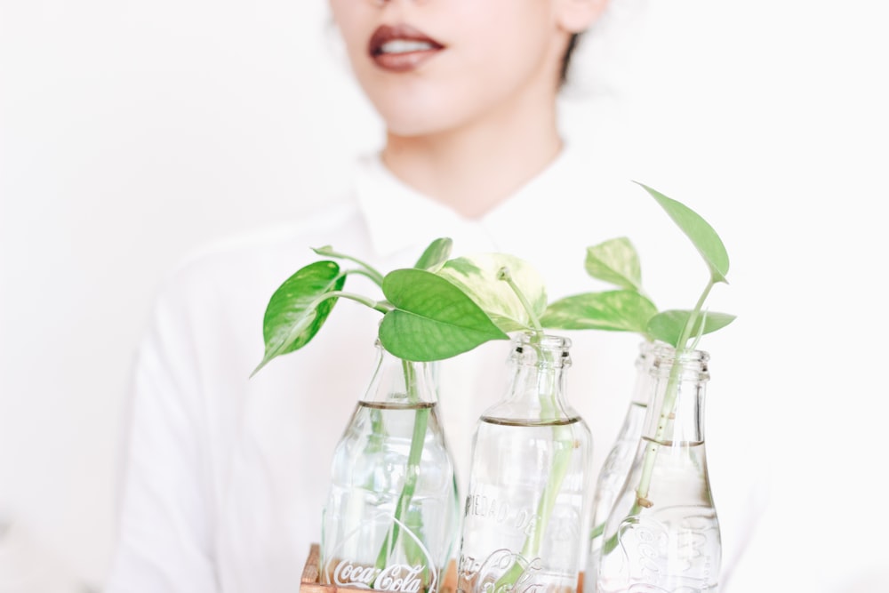 uma mulher segurando três garrafas de coca-cola vazias com plantas nelas