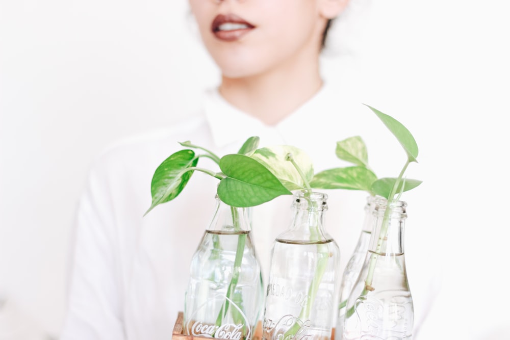 a woman holding three empty coke bottles with plants in them