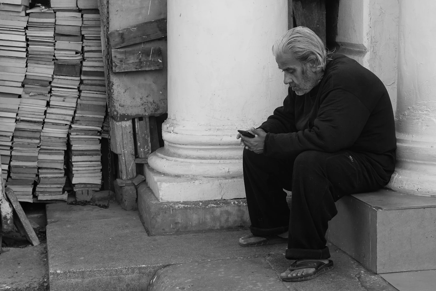 Young man sitting beside a stone pillar searching on his smartphone