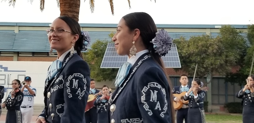 A vibrant mariachi band playing energetically outdoors with smiling attendees dancing nearby.