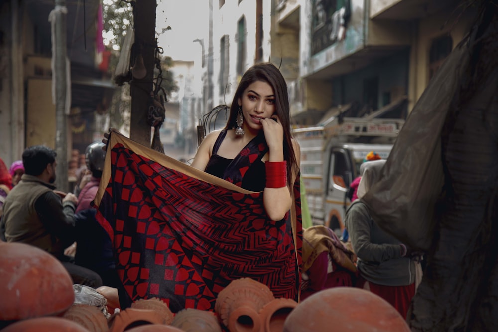 Femme debout tenant un textile rouge et noir près de personnes et de véhicules