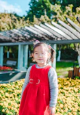 A cheerful toddler wearing a sunny yellow crochet dress, playing in a garden filled with blooming flowers.
