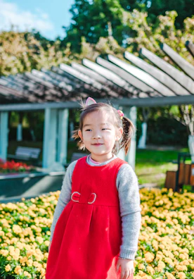 A cheerful toddler wearing a sunny yellow crochet dress, playing in a garden filled with blooming flowers.