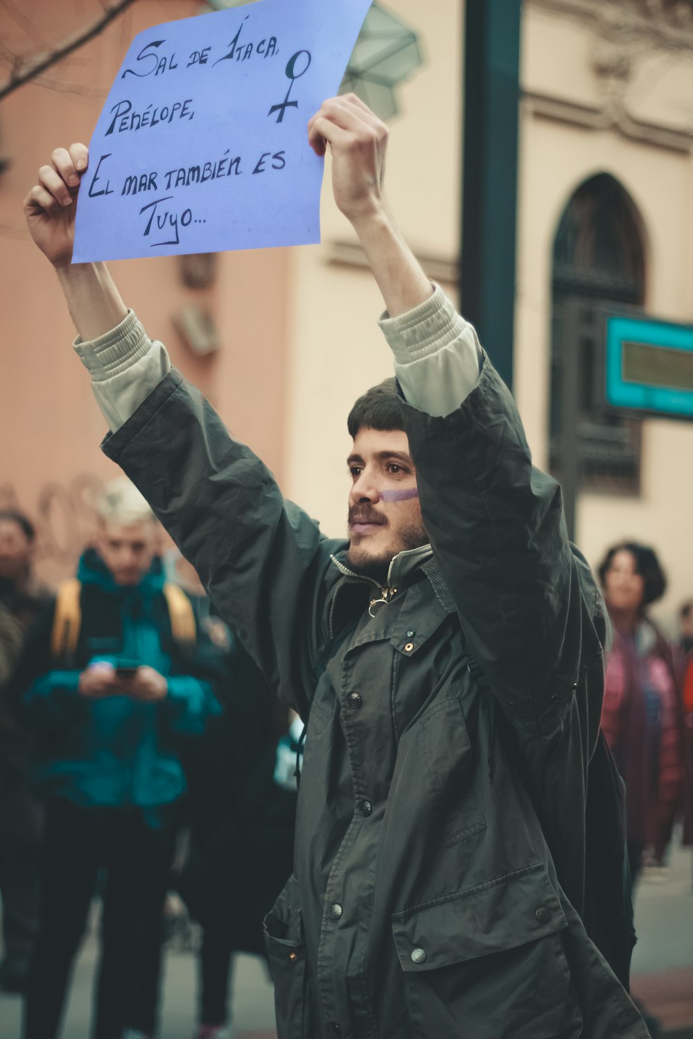 man in grey jacket holding blue placard