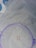 A piece of light-colored fabric with small pink rose patterns and green leaves embroidered on it. A purple embroidery hoop is partially shown, used to hold the fabric taut.