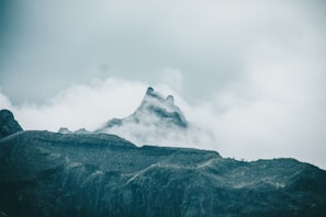 A dramatic mountain peak piercing through swirling mist under a moody sky.