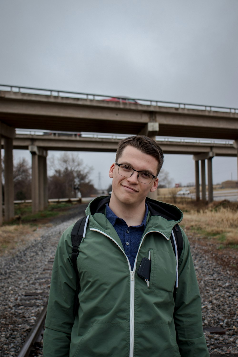 man wearing green zip-up jacket standing near bridge during daytime