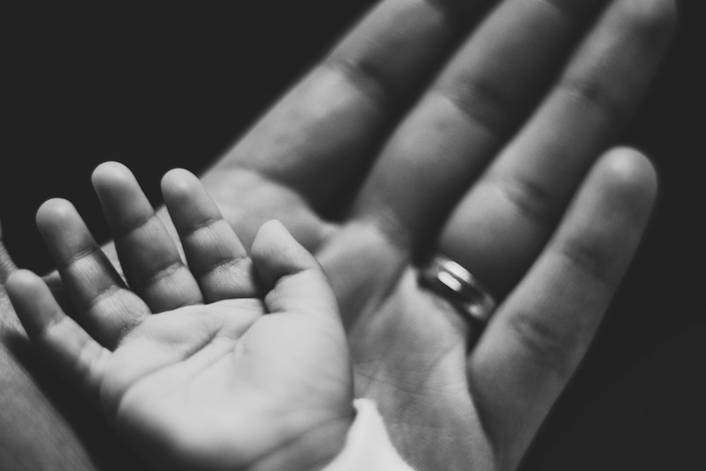 grayscale photography of baby's palm on adult