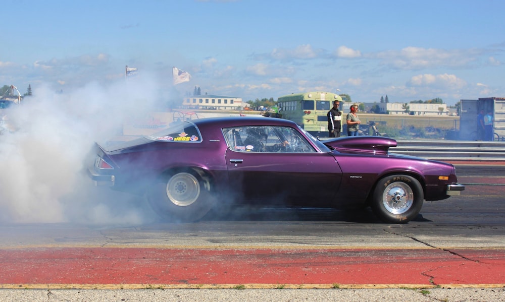 purple coupe burning out on road during daytime