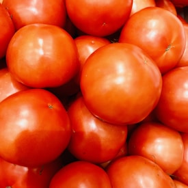 A large pile of fresh, ripe tomatoes with smooth, shiny red skins. The lighting highlights their plumpness and freshness.
