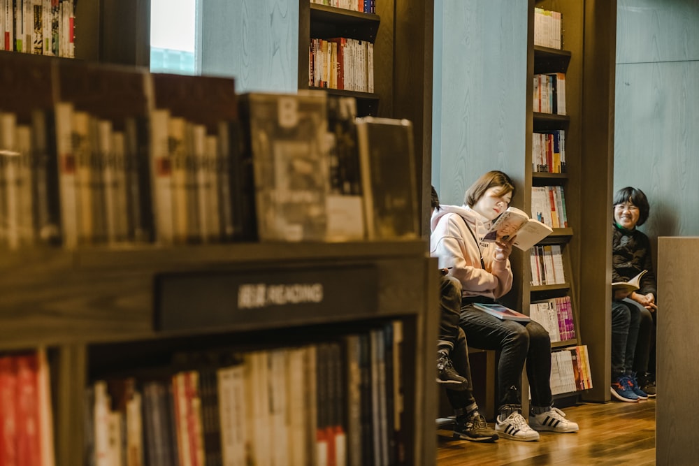 woman holding book leaning on shelf