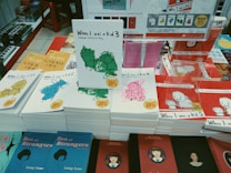A display of various books on a table, featuring multiple copies of a series titled 'When I was a kid' with different volume numbers and cover illustrations in green, pink, blue, and yellow. Each book has a 20% discount sticker. Other visible titles include 'Sea of Strangers' by Lang Leav, and there are book cover images of various styles visible in the background.